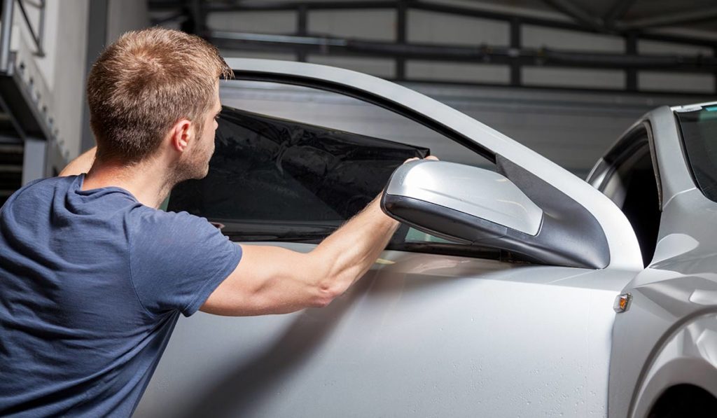 Mann bringt getönte Folie an Autofenster an.