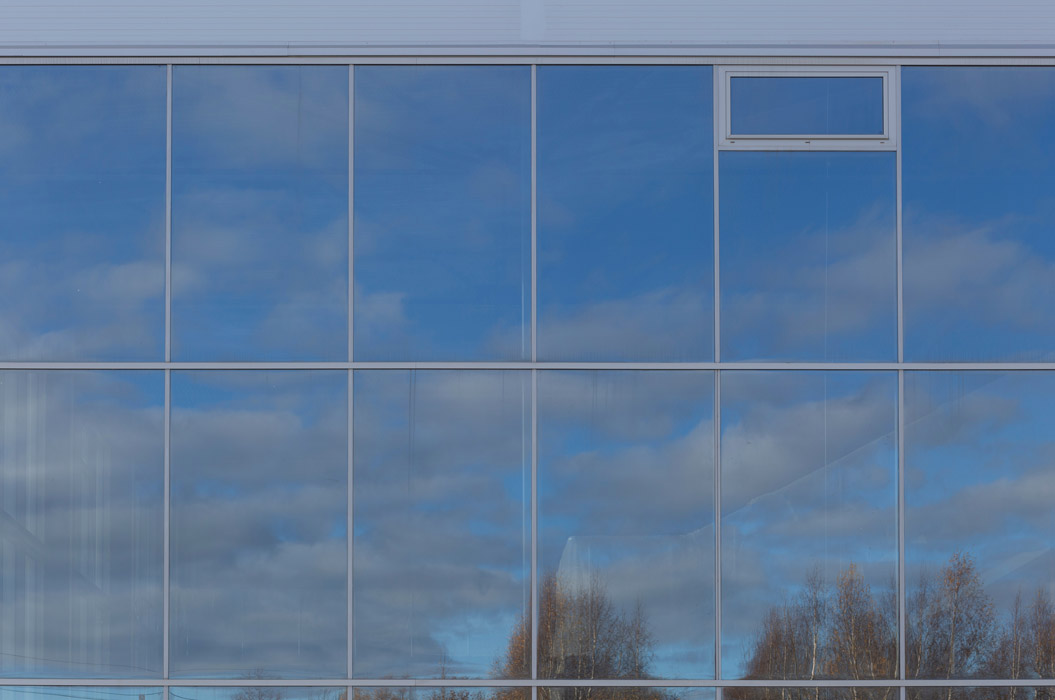 
Fassade aus Glas mit Tönungsfolien. Blauer Himmel und Wolken spiegeln sich